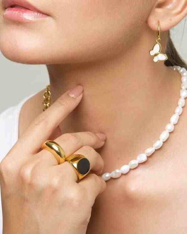 Lifestyle shot featuring a model's hand resting on a gold necklace, showcasing the Domsley chunky gold wedding band dome ring stacked with other gold-plated jewelry.