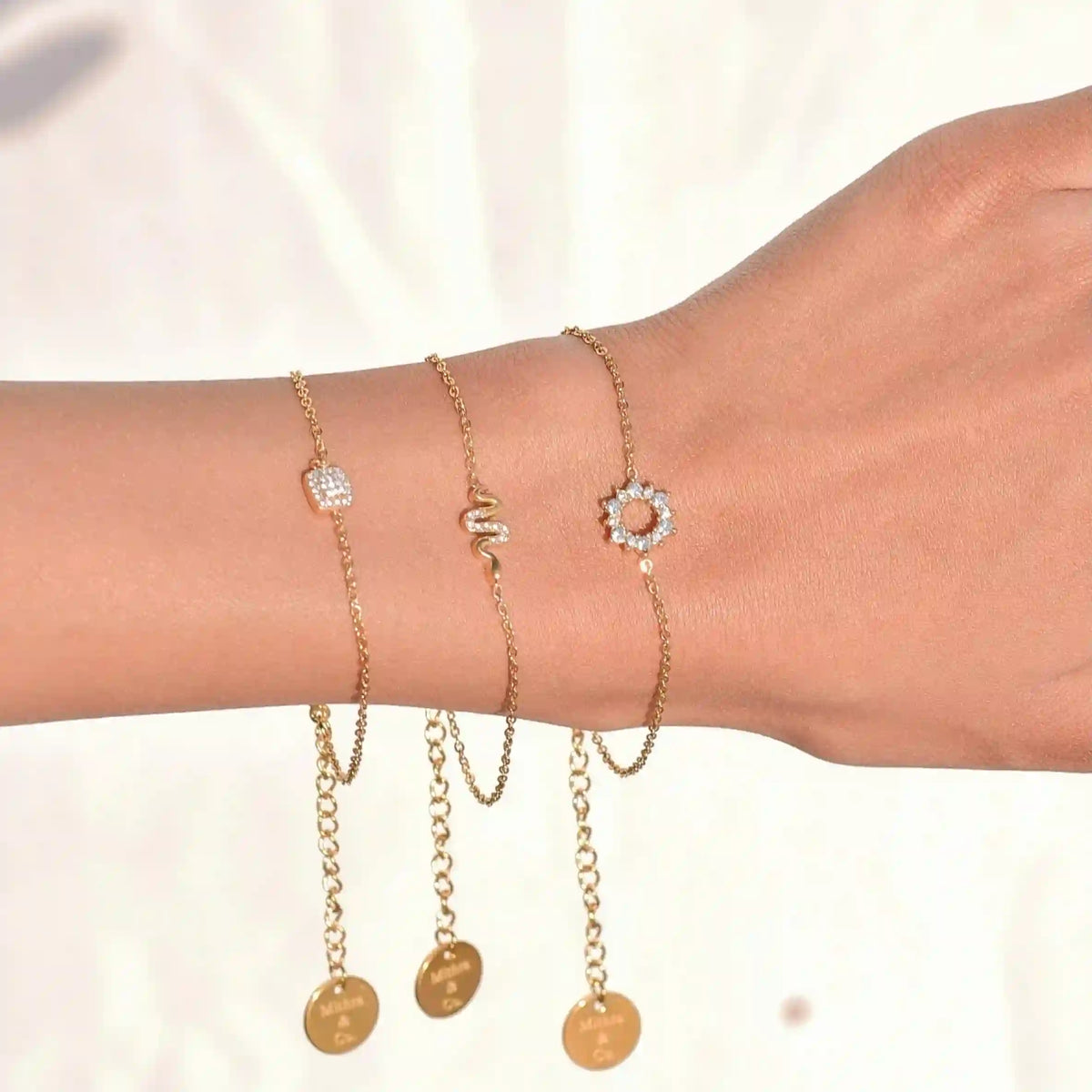 Closeup of a woman's hand wearing 18k Gold Plated Petit Bracelets including Pave Slither Snake Motif Danity chain Bracelet Adorned with Zircons.