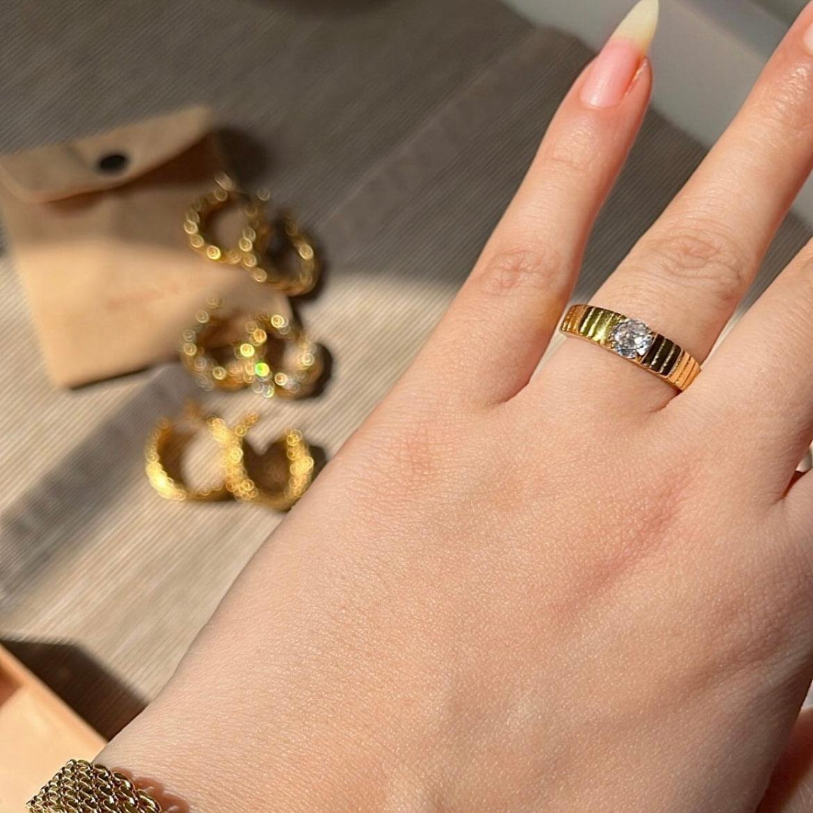 Closeup of a hand wearing bowie ring industrial  style CZ ring in ring finger with 6 other rings and a pouch blurred in bg. Shop at Mithra and Co