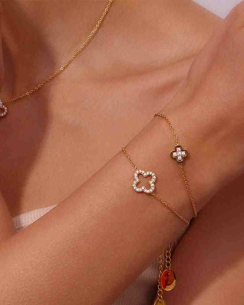 Closeup of a wrist and neck wearing Hollow clover studded Bracelet and Necklace. Featuring Open-Silhouette Quatrefoil handchain design with Pave Zircon Layering.