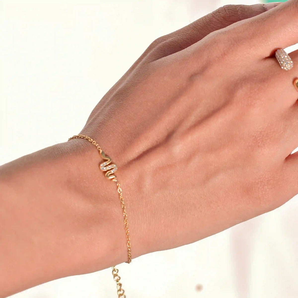 Closeup of a woman's hand wearing petit snake motif bracelet. 18k gold plated Pavé Slither danity hand chain.